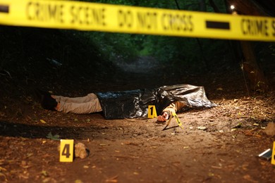 Photo of Forensic expertise. Crime scene with dead man's body and markers outdoors