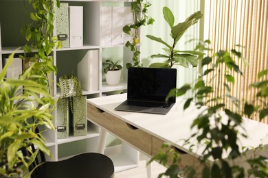 Photo of Biophilic interior design. Stylish workplace with laptop and houseplants in office