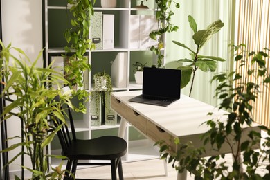 Photo of Biophilic interior design. Stylish workplace with laptop and houseplants in office