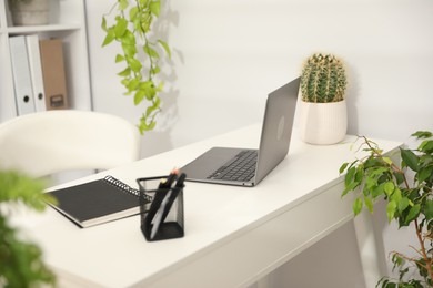 Photo of Stylish workplace with laptop, stationery and floral decor in office. Biophilic interior design