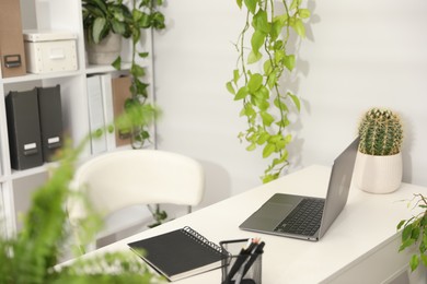 Photo of Stylish workplace with laptop, stationery and floral decor in office. Biophilic interior design