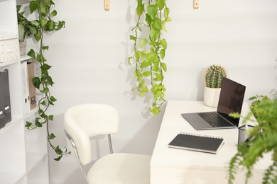 Photo of Stylish workplace with laptop, stationery and floral decor in office. Biophilic interior design