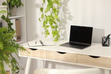 Photo of Stylish workplace with laptop, stationery and floral decor in office. Biophilic interior design
