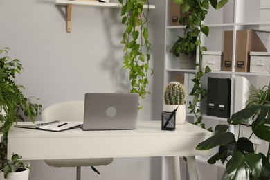 Photo of Stylish workplace with laptop, stationery and floral decor in office. Biophilic interior design