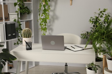 Photo of Stylish workplace with laptop, stationery and floral decor in office. Biophilic interior design
