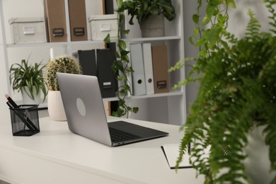 Photo of Stylish workplace with laptop, stationery and floral decor in office. Biophilic interior design