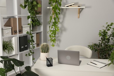 Photo of Stylish workplace with laptop, stationery and floral decor in office. Biophilic interior design