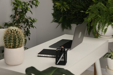 Photo of Stylish workplace with laptop, stationery and floral decor in office. Biophilic interior design