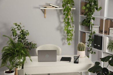 Photo of Stylish workplace with laptop, stationery and floral decor in office. Biophilic interior design
