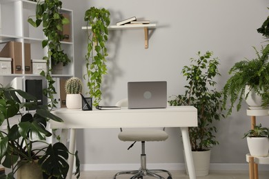 Photo of Stylish workplace with laptop, stationery and floral decor in office. Biophilic interior design