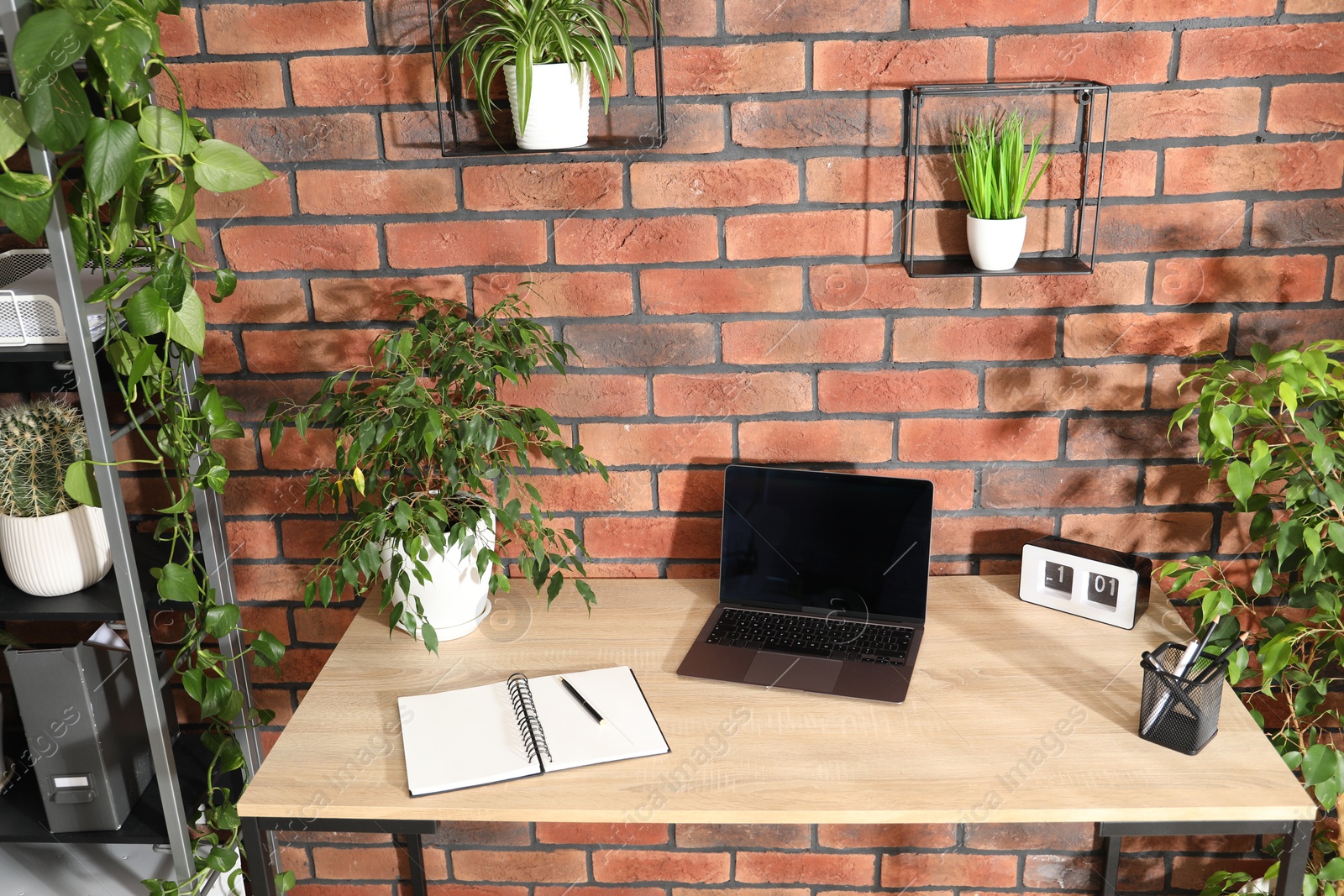 Stylish workplace with laptop, stationery and floral decor in office. Biophilic interior design Photo of Stylish workplace with laptop, stationery and floral decor in office. Biophilic interior design