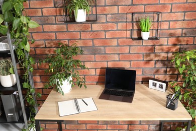 Photo of Stylish workplace with laptop, stationery and floral decor in office. Biophilic interior design