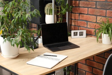Photo of Stylish workplace with laptop, stationery and floral decor in office. Biophilic interior design