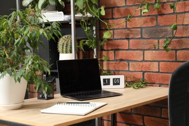 Photo of Stylish workplace with laptop, stationery and floral decor in office. Biophilic interior design
