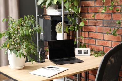 Photo of Stylish workplace with laptop, stationery and floral decor in office. Biophilic interior design