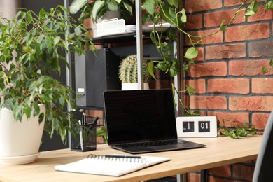 Photo of Stylish workplace with laptop, stationery and floral decor in office. Biophilic interior design
