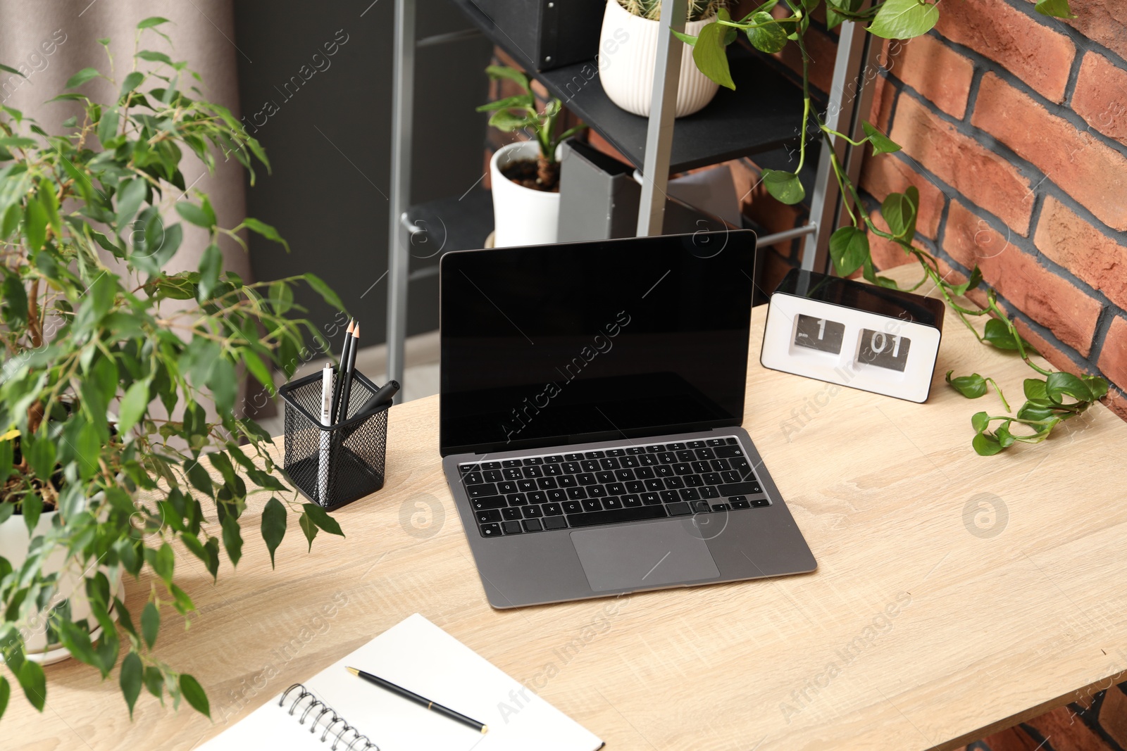 Stylish workplace with laptop, stationery and floral decor in office. Biophilic interior design Photo of Stylish workplace with laptop, stationery and floral decor in office. Biophilic interior design