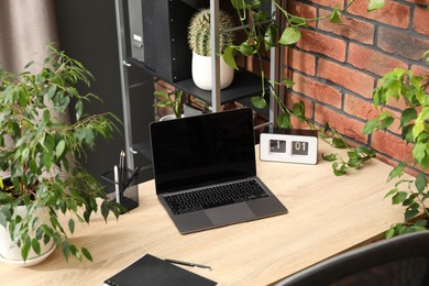 Photo of Stylish workplace with laptop, stationery and floral decor in office. Biophilic interior design