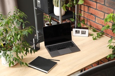 Photo of Stylish workplace with laptop, stationery and floral decor in office. Biophilic interior design
