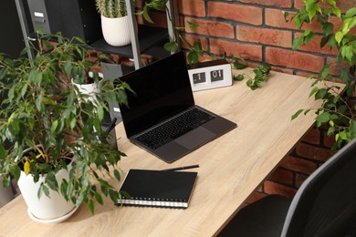 Photo of Stylish workplace with laptop, stationery and floral decor in office. Biophilic interior design