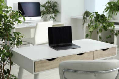 Photo of Stylish workplace with laptop, modern computer and floral decor in office. Biophilic interior design