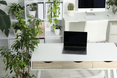 Photo of Stylish workplace with laptop, modern computer and floral decor in office. Biophilic interior design