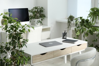 Photo of Stylish workplace with laptop, stationery and floral decor in office. Biophilic interior design