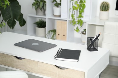 Photo of Stylish workplace with laptop, stationery and floral decor in office. Biophilic interior design