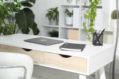 Photo of Stylish workplace with laptop, stationery and floral decor in office. Biophilic interior design