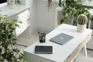 Photo of Stylish workplace with laptop, stationery and floral decor in office. Biophilic interior design