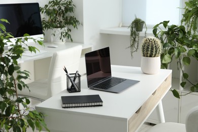 Photo of Stylish workplace with laptop, stationery and floral decor in office. Biophilic interior design