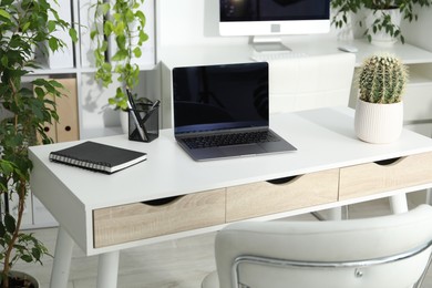 Photo of Stylish workplace with laptop, stationery and floral decor in office. Biophilic interior design
