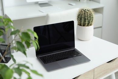 Photo of Stylish workplace with laptop, stationery and floral decor in office. Biophilic interior design