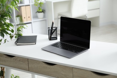 Photo of Stylish workplace with laptop, stationery and floral decor in office. Biophilic interior design