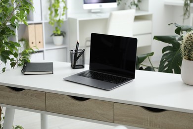 Photo of Stylish workplace with laptop, stationery and floral decor in office. Biophilic interior design