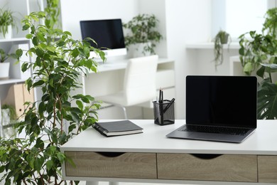 Photo of Stylish workplace with laptop, stationery and floral decor in office. Biophilic interior design