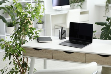 Photo of Stylish workplace with laptop, stationery and floral decor in office. Biophilic interior design
