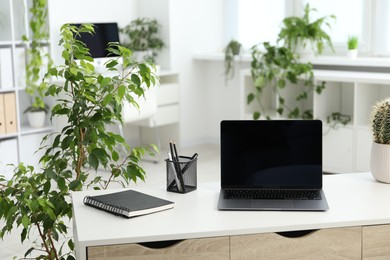 Photo of Stylish workplace with laptop, stationery and floral decor in office. Biophilic interior design