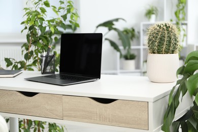 Photo of Stylish workplace with laptop, stationery and floral decor in office. Biophilic interior design