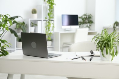 Photo of Stylish workplace with laptop, stationery and floral decor in office. Biophilic interior design