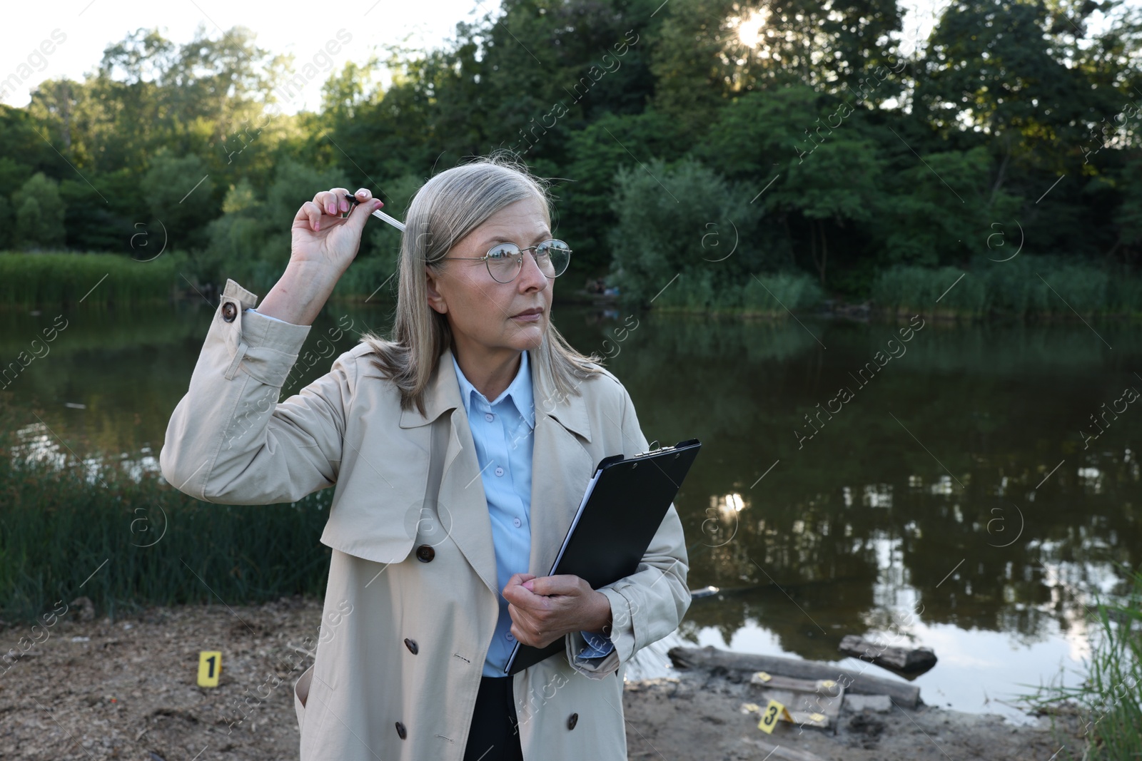 Photo of Forensic expertise. Detective with clipboard at crime scene near lake outdoors, space for text