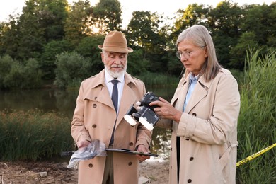 Photo of Forensic expertise. Detectives working at crime scene near lake outdoors
