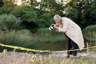 Photo of Forensic expertise. Detective with camera working at crime scene near lake outdoors, space for text