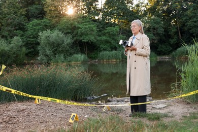 Photo of Forensic expertise. Detective with camera working at crime scene near lake outdoors, space for text