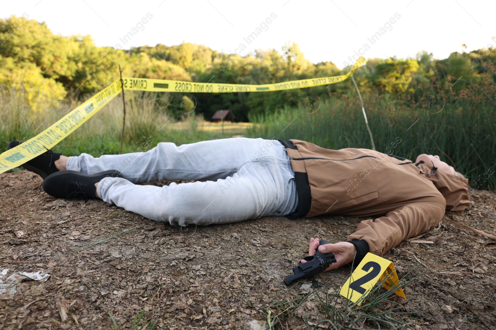 Photo of Forensic expertise. Crime scene with dead man's body, gun and marker outdoors
