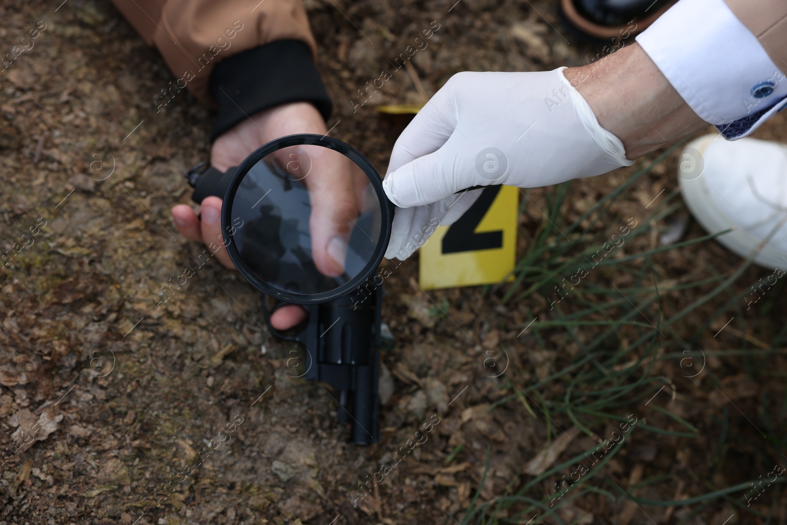 Photo of Forensic expertise. Detective with magnifying glass working at crime scene with dead man's body outdoors, above view