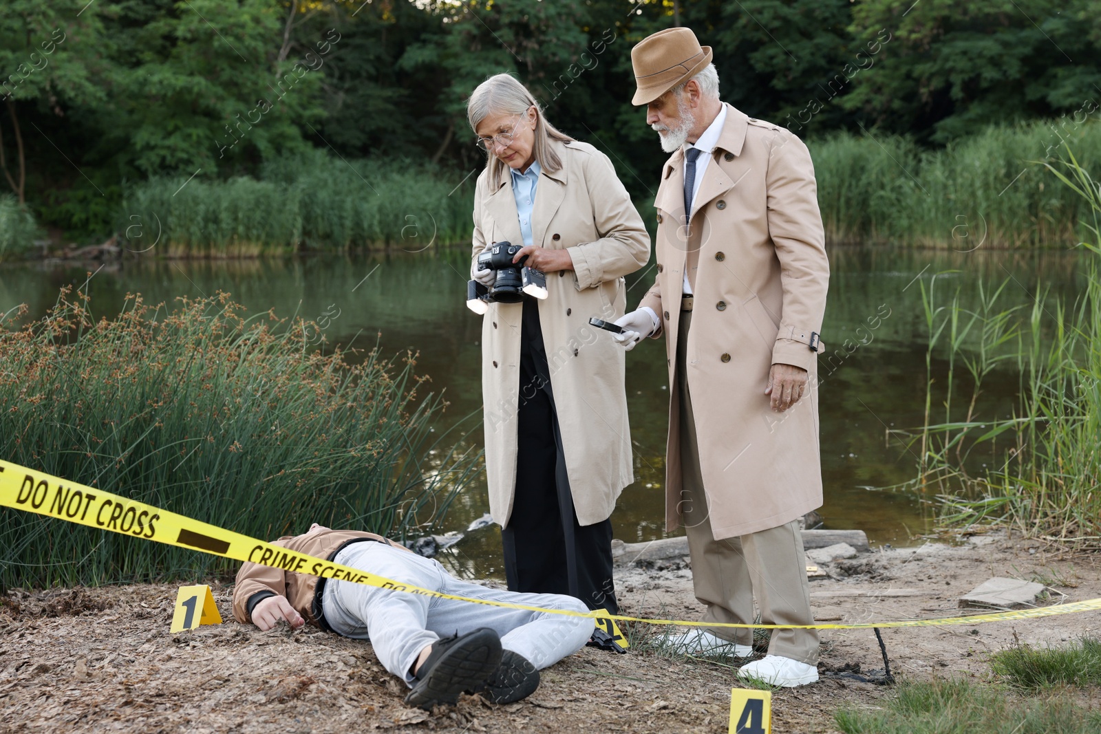 Photo of Forensic expertise. Detectives working at crime scene with dead man's body near lake outdoors
