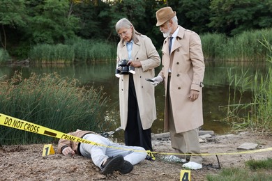 Photo of Forensic expertise. Detectives working at crime scene with dead man's body near lake outdoors