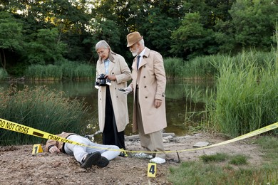 Photo of Forensic expertise. Detectives working at crime scene with dead man's body near lake outdoors