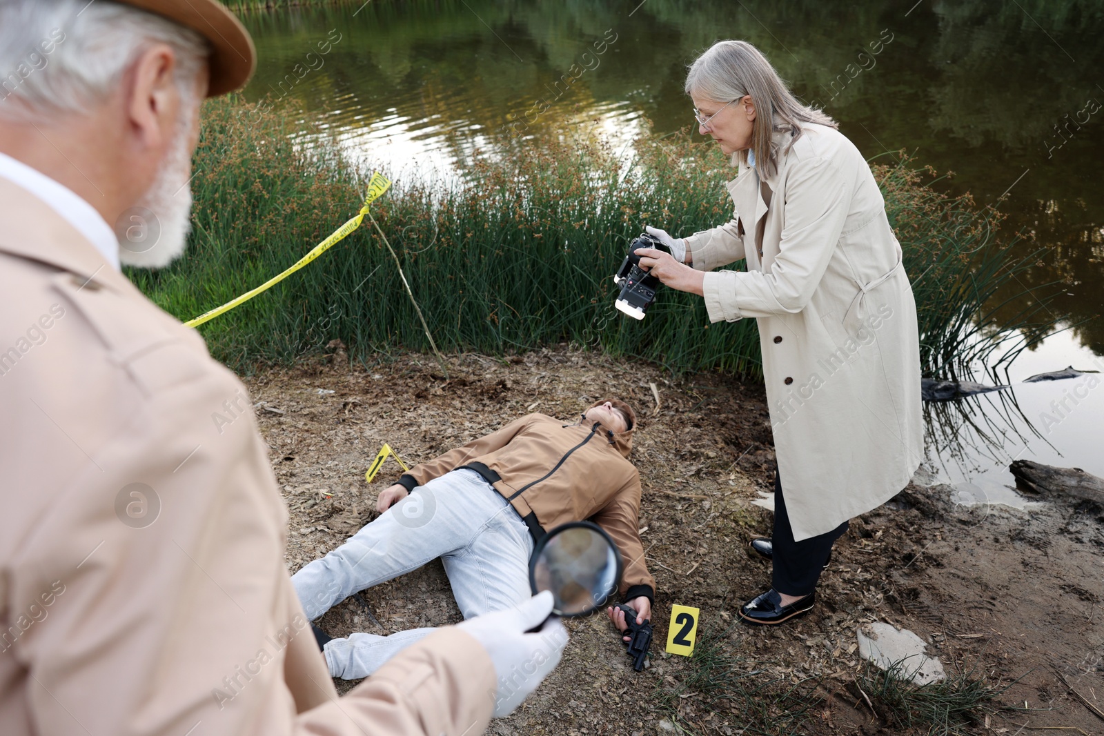 Photo of Forensic expertise. Detectives working at crime scene with dead man's body near lake outdoors
